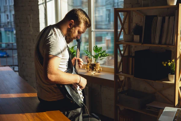 Músico caucásico tocando la guitarra durante concierto en línea en casa aislado y en cuarentena, improvisación impresionante a la luz del sol — Foto de Stock