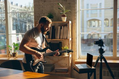 Beyaz müzisyen evdeki online konser sırasında gitar çalıyor izole ve karantinaya alınmış, etkileyici bir doğaçlama.