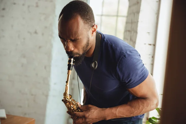 African-american musician playing saxophone during online concert at home isolated and quarantined, attented, focused