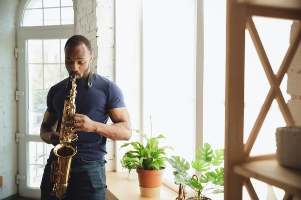 Músico afroamericano tocando saxofón durante concierto en línea en casa aislado y en cuarentena, atento, enfocado — Foto de Stock