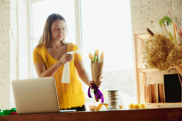 Florista en el trabajo: la mujer muestra cómo hacer ramo con tulipanes, trabajando en el concepto de casa, usando aerosol — Foto de Stock