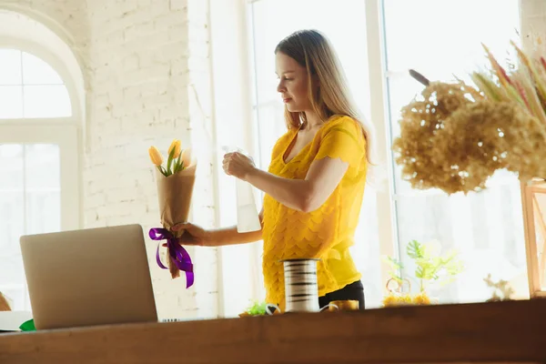 Floristin bei der Arbeit: Frau zeigt, wie man Strauß mit Tulpen macht, zu Hause arbeitet, Blumen zubereitet — Stockfoto