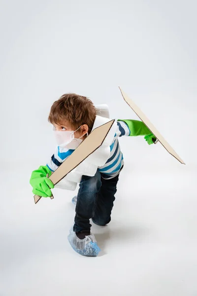 Pequeño chico caucásico como guerrero en lucha contra la pandemia de coronavirus, con un escudo, una espada y un bandolero de papel higiénico, atacando — Foto de Stock