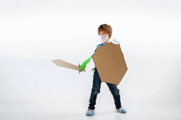 Pequeño chico caucásico como guerrero en lucha contra la pandemia de coronavirus, con un escudo, una espada y un pañuelo de papel higiénico, protegiendo —  Fotos de Stock