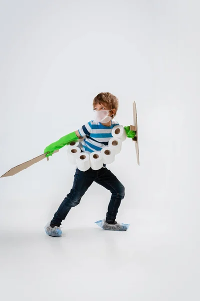 Pequeño chico caucásico como guerrero en lucha contra la pandemia de coronavirus, con un escudo, una espada y un pañuelo de papel higiénico, protegiendo — Foto de Stock