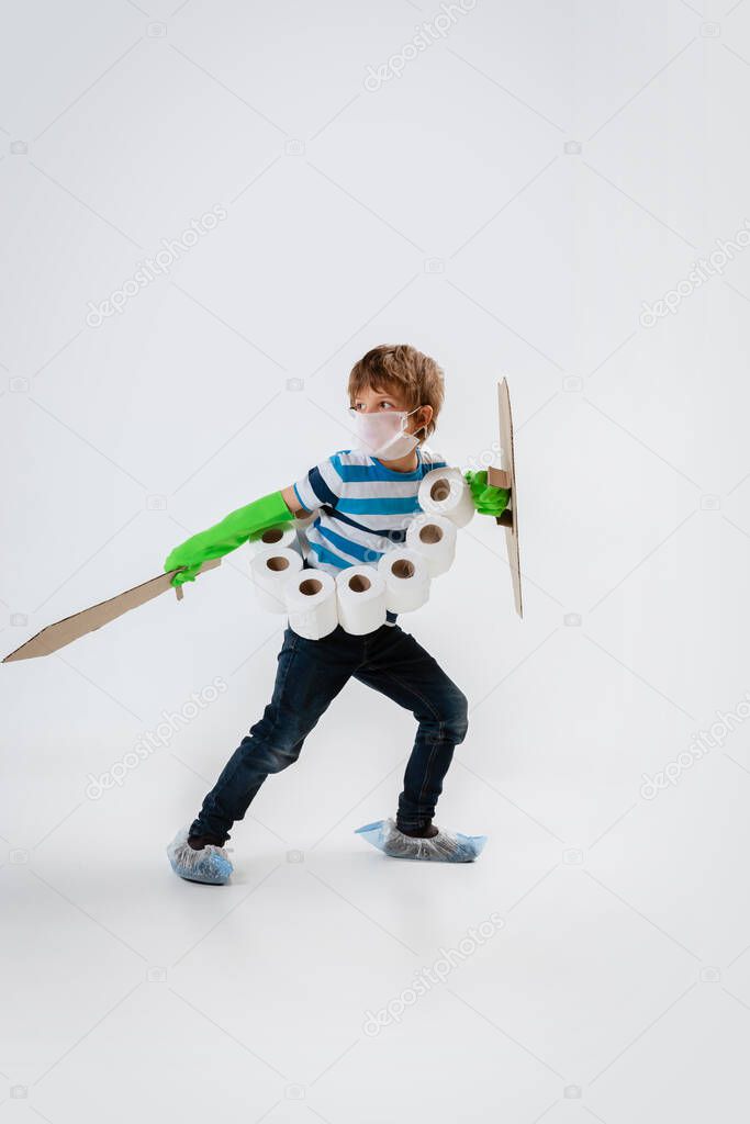 Little caucasian boy as a warrior in fight with coronavirus pandemic, with a shield, a sword and a toilet paper bandoleer, protecting