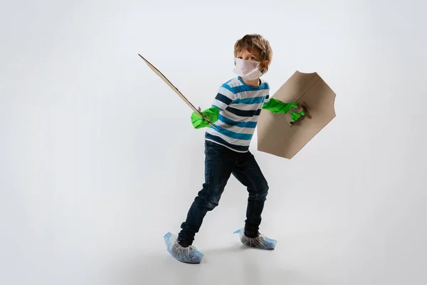 Mały biały chłopiec jako wojownik w walce z pandemią koronawirusów, z tarczą, mieczem i bandoleerem papieru toaletowego, chroniący — Zdjęcie stockowe