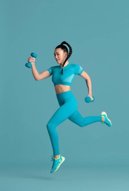 Güzel genç bayan atlet mavi stüdyo arka planında pratik yapıyor, tek renkli portre.