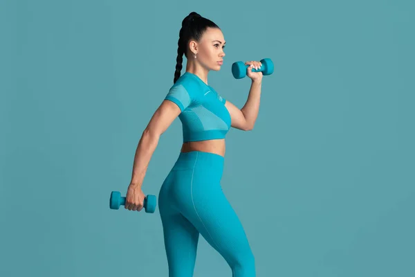 Beautiful young female athlete practicing on blue studio background, monochrome portrait — Stock Photo, Image