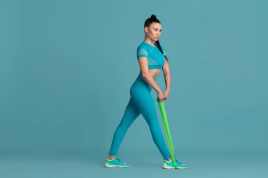 Güzel genç bayan atlet mavi stüdyo arka planında pratik yapıyor, tek renkli portre.