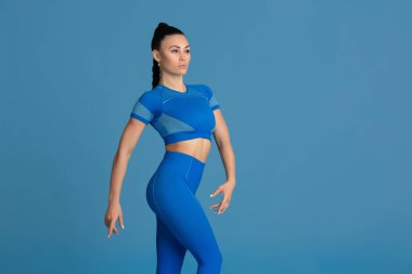 Güzel genç bayan atlet mavi stüdyo arka planında pratik yapıyor, tek renkli portre.