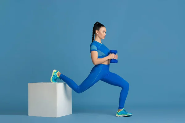 Krásná mladá žena sportovec cvičení na modrém pozadí studia, monochromatický portrét — Stock fotografie