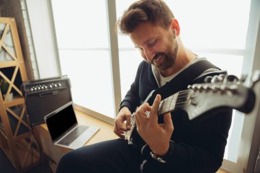 Beyaz müzisyen evdeki online konser sırasında gitar çalıyor izole edilmiş ve karantinaya alınmış, neşeli doğaçlama