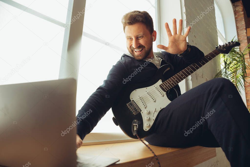 Caucasian musician playing guitar during concert at home isolated and quarantined, cheerful improvising with the band connected online
