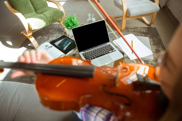 Young woman studying at home during online courses or free information by herself, playing violin, improvising