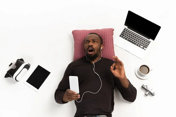 Эмоциональный афро-американец, использующий телефон, окруженный устройствами, изолированными на белом фоне студии, технологиями, соединяющими людей. Вдохновленное пение — стоковое фото