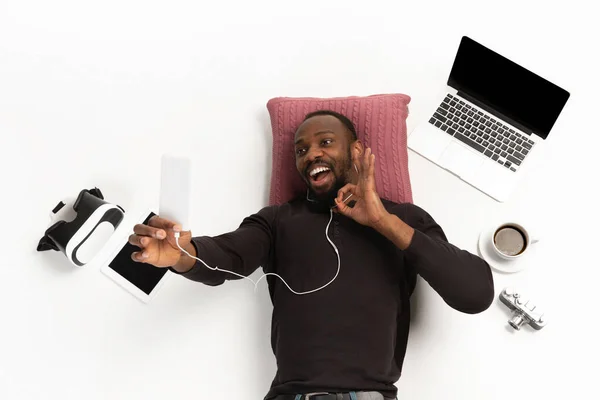 Эмоциональный афро-американец, использующий телефон, окруженный устройствами, изолированными на белом фоне студии, технологиями, соединяющими людей. Онлайн встреча, селфи — стоковое фото