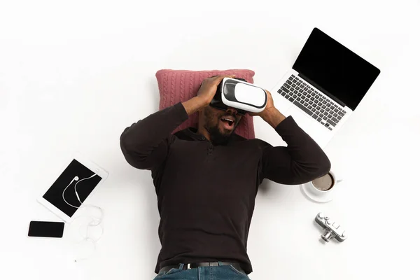 Homme afro-américain émotionnel utilisant VR-casque entouré de gadgets isolés sur fond de studio blanc, technologies. Jeu émotionnel — Photo