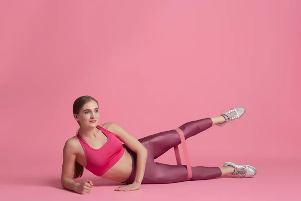 Schöne junge Sportlerin übt auf rosa Studiohintergrund, monochromes Porträt — Stockfoto