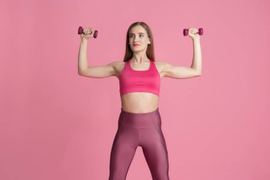 Pembe stüdyo arka planında pratik yapan güzel genç bayan sporcu, tek renkli portre.