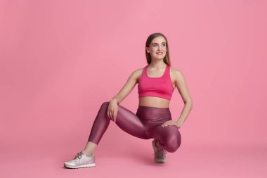 Pembe stüdyo arka planında pratik yapan güzel genç bayan sporcu, tek renkli portre.