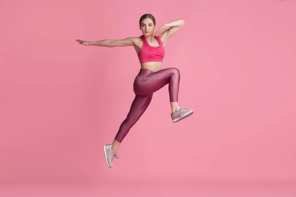 Schöne junge Sportlerin übt auf rosa Studiohintergrund, monochromes Porträt — Stockfoto