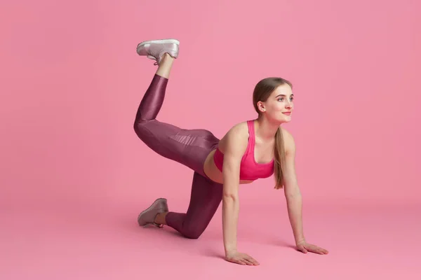 Schöne junge Sportlerin übt auf rosa Studiohintergrund, monochromes Porträt — Stockfoto