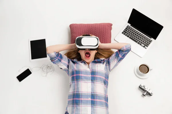 Эмоциональная кавказка, использующая VR-headsed, окруженная устройствами, изолированными на белом студийном фоне, технологиями. Шокирован, напуган — стоковое фото
