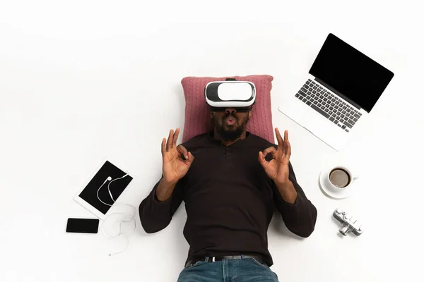 Homme afro-américain émotionnel utilisant VR-casque entouré de gadgets isolés sur fond de studio blanc, technologies. Gentil, heureux — Photo