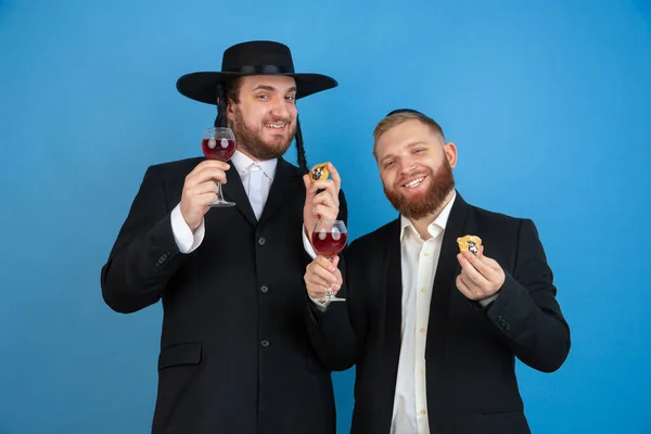 Portrait of a young orthodox jewish men isolated on blue studio background, meeting the Passover, eating Amans ears with wine — Stock Photo, Image