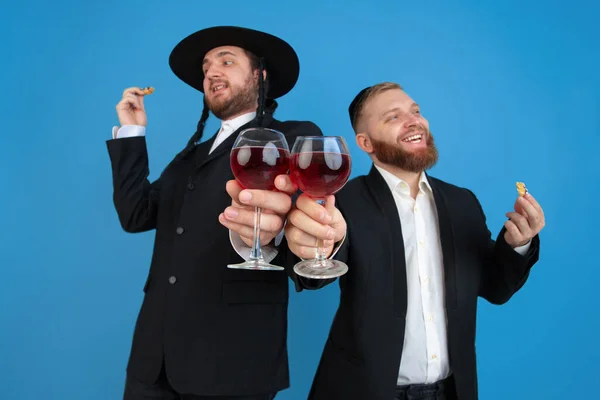 Porträt eines jungen orthodoxen jüdischen Mannes isoliert auf blauem Studiohintergrund, der das Pessach trifft und Amans Ohren mit Wein verspeist — Stockfoto