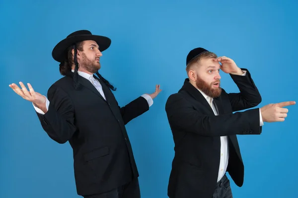 Portré egy fiatal ortodox zsidó férfiak elszigetelt kék stúdió háttér, találkozás a páska-ünnep, csodálkozva — Stock Fotó