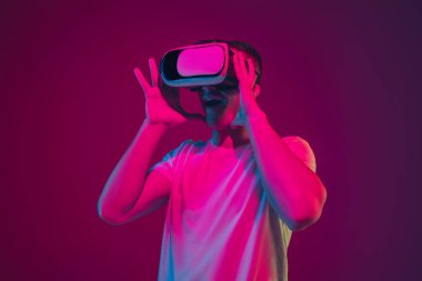 Beyaz adam portresi pembe-mor stüdyo arka planında, neon ışıkta izole edilmiş, VR-kulaklıkla oynuyor.