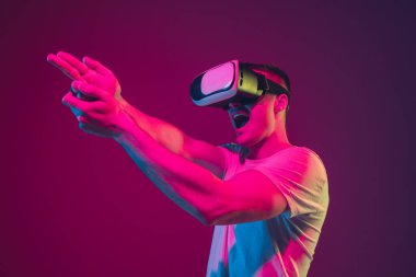 Caucasian mans portrait isolated on pink-purple studio background in neon light, playing with VR-headset clipart