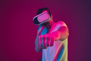 Beyaz adam portresi pembe-mor stüdyo arka planında, neon ışıkta izole edilmiş, VR-kulaklıkla oynuyor.