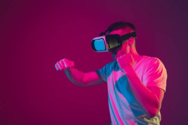 Beyaz adam portresi pembe-mor stüdyo arka planında, neon ışıkta izole edilmiş, VR-kulaklıkla oynuyor.