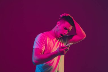 Beyaz adam portresi pembe-mor stüdyo arka planında izole edilmiş, neon ışıkta, tablet kullanılarak.