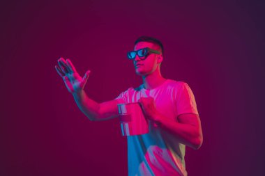 Beyaz adam portresi pembe-mor stüdyo arka planında, neon ışıkta izole edilmiş, 3D sinema gözlüğü takıyor.