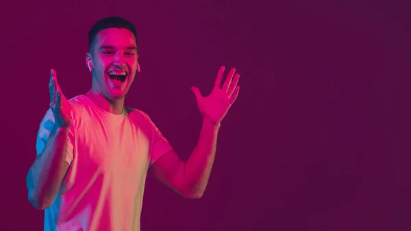 Portrait homme caucasien isolé sur fond studio rose-violet à la lumière néon, à l'aide d'écouteurs sans fil — Photo