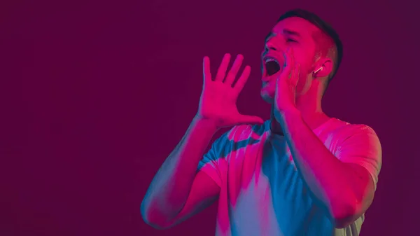 Retrato de homem caucasiano isolado em fundo de estúdio rosa-roxo em luz de néon, usando fones de ouvido sem fio — Fotografia de Stock