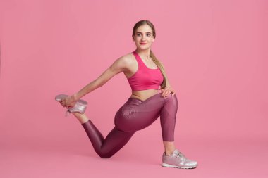 Pembe stüdyo arka planında pratik yapan güzel genç bayan sporcu, tek renkli portre.