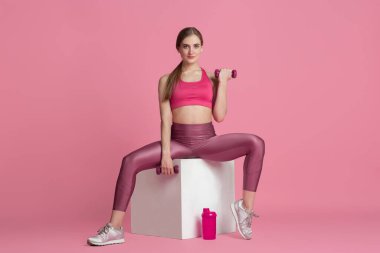 Pembe stüdyo arka planında pratik yapan güzel genç bayan sporcu, tek renkli portre.