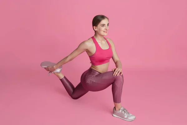 Schöne junge Sportlerin übt auf rosa Studiohintergrund, monochromes Porträt — Stockfoto