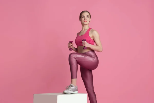 아름다운 젊은 여성 운동 선수가 분홍색 스튜디오 배경, 모노크롬 초상화를 입고 연습하고 있습니다. — 스톡 사진