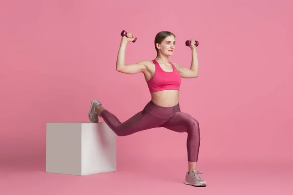 Schöne junge Sportlerin übt auf rosa Studiohintergrund, monochromes Porträt — Stockfoto