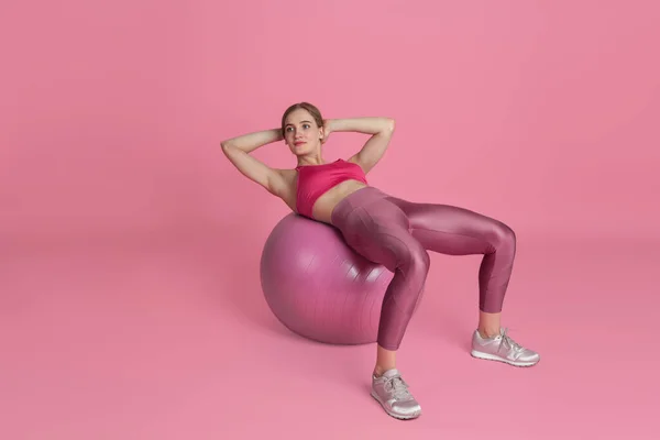 Schöne junge Sportlerin übt auf rosa Studiohintergrund, monochromes Porträt — Stockfoto