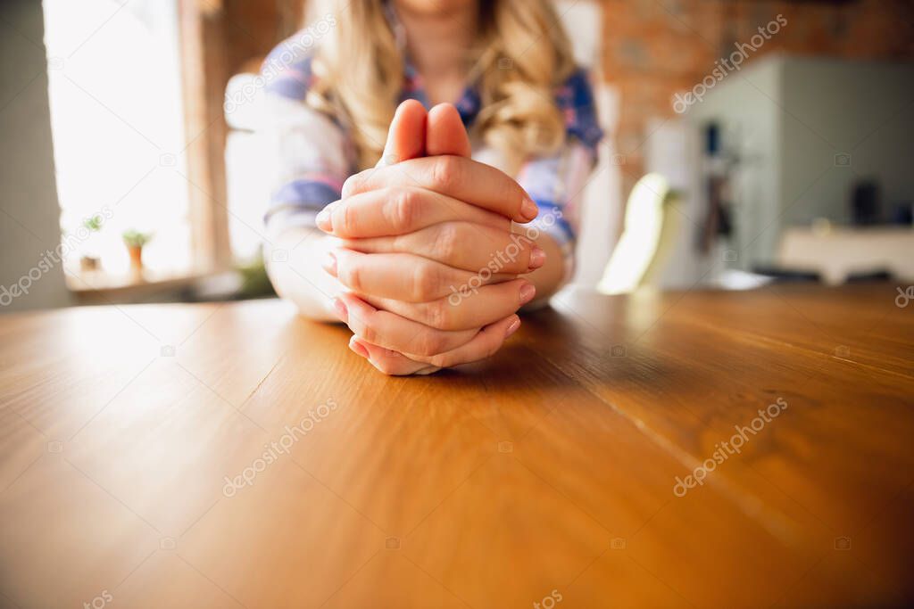 Woman sitting at the table with her hands folded, close up