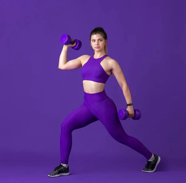 Piękna młoda atletka ćwicząca na fioletowym tle studia, monochromatyczny portret — Zdjęcie stockowe