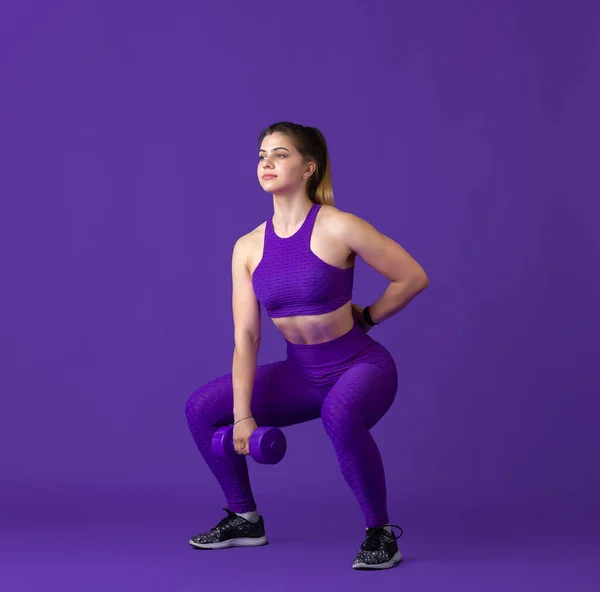 漂亮的年轻女运动员在紫色工作室背景，单色肖像上练习 — 图库照片