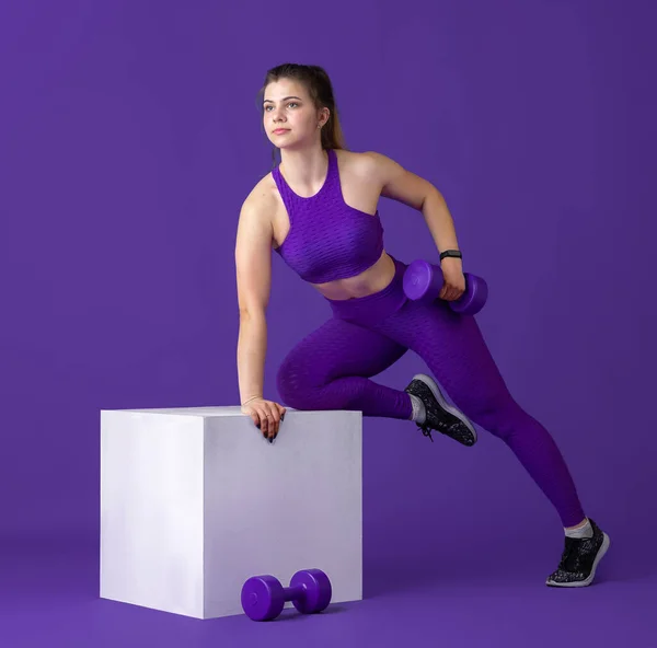 Bella giovane atleta femminile che pratica su sfondo viola studio, ritratto monocromatico — Foto Stock